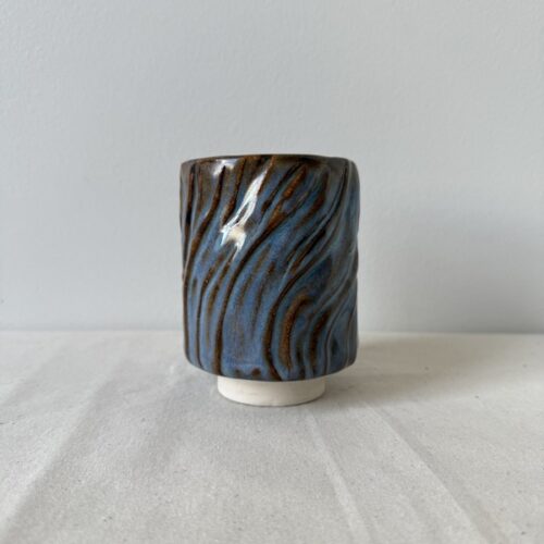 ceramic japanese footed teacup with waves in randys red brown glaze on neutral linen fabric and cream wall background by studio hon handbuilding pottery