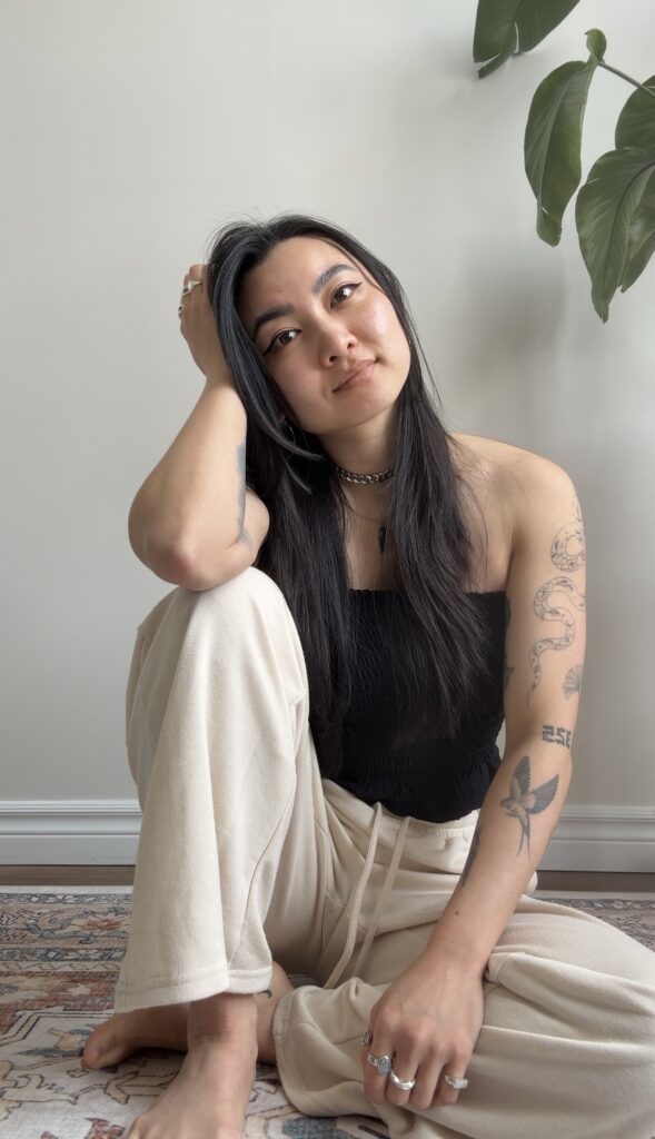 suki hon of studio hon headshot seated on rug against white wall and slight foliage in right hand corner